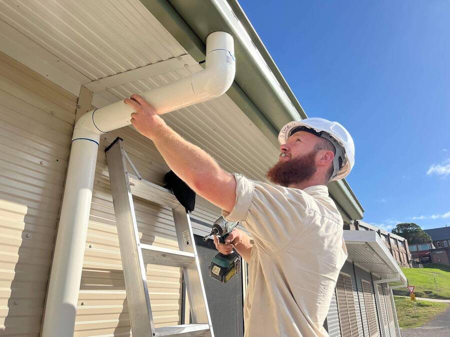 Aidan, licensed plumber and gasfitter, fitting a new downpipe at the eaves of a commercial building