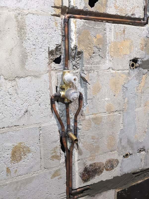 Copper hot and cold pipework and a shower mixer body chased into a block wall during a bathroom rough-in