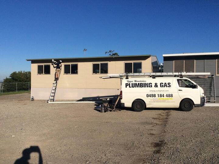 Upper Mountains Plumbing and Gas van parked at a demountable building, with a ladder up at the eaves and lengths of new guttering on the ground