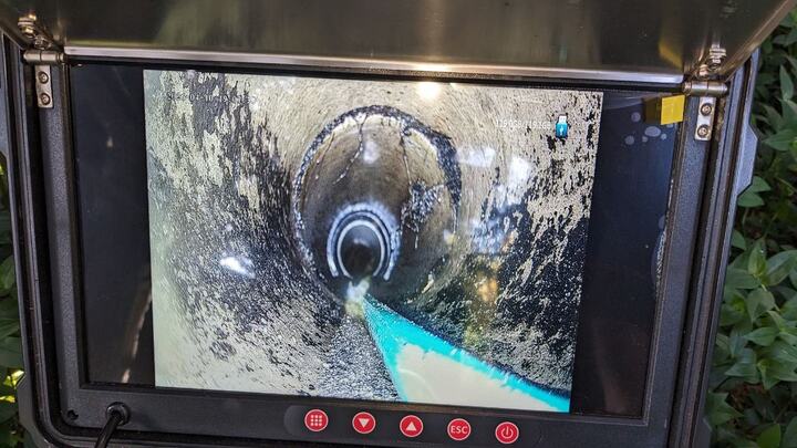 A drain camera monitor in a hinged case showing the inside of a pipe, with a mortared joint collar part way along, build-up on the pipe wall and the camera skid in the bottom of the frame