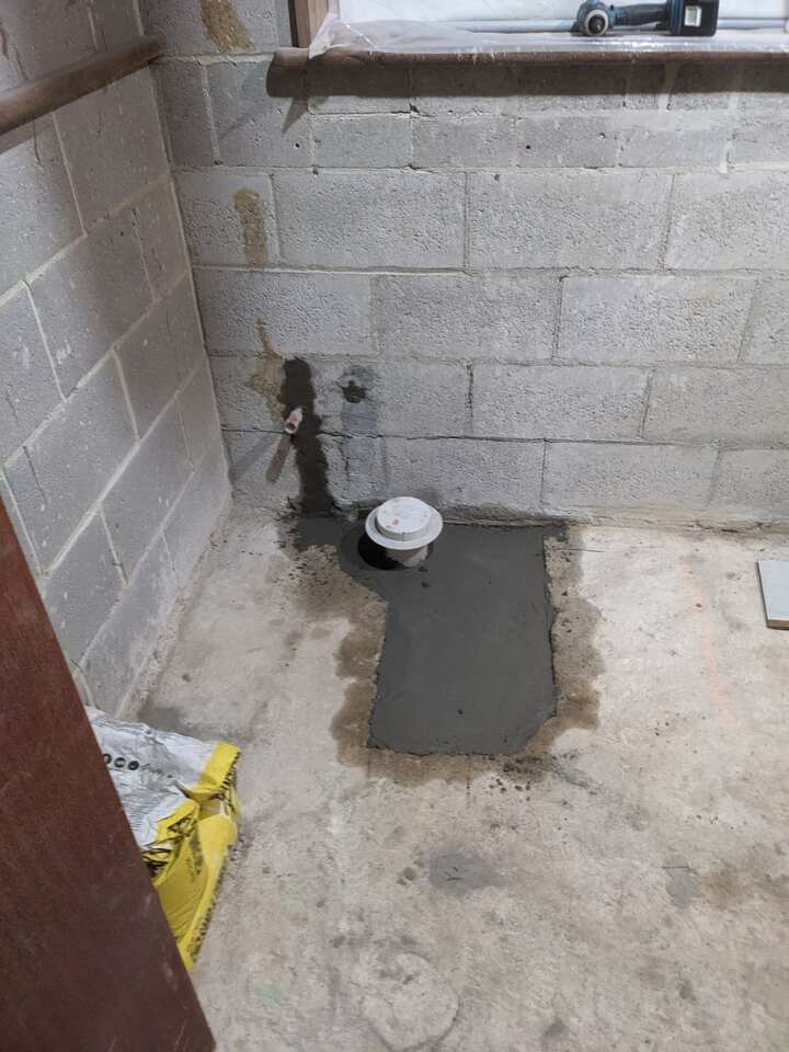 Waste outlet set in fresh mortar in a concrete floor, with pipework chased into the block wall behind it