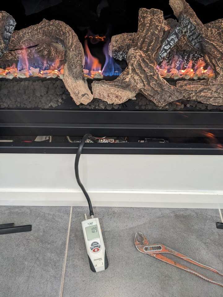 Gas log fire alight, with a manometer connected to the appliance test point and a set of multigrips on the floor