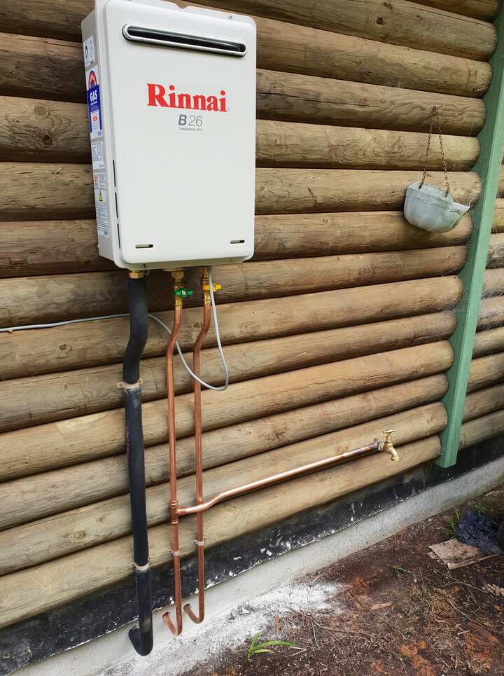 Rinnai B26 continuous flow gas hot water unit on an external timber wall, with copper pipework and isolation valves below it