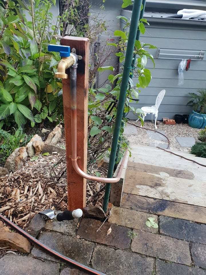 New copper garden standpipe fixed to a hardwood post, with a brass lever-handle hose tap at the top
